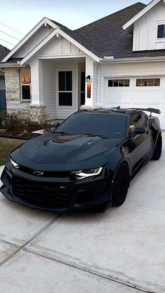 a black chevrolet camaro parked in front of a house