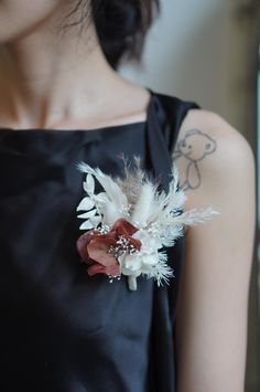 a woman wearing a black dress with white flowers and feathers attached to her back shoulder