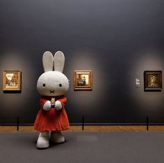 a large stuffed rabbit sitting on top of a floor in front of some framed pictures