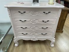 a white chest of drawers sitting on top of a wooden floor next to a glass case