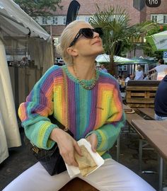 a woman sitting at a table with a sandwich in her hand and looking up into the sky