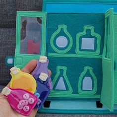 a hand is holding a small toy in front of a doll's play house