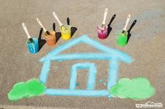 some paint and brushes are sitting in the sand with a house drawn on it's side