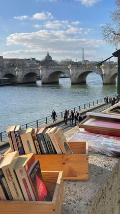 there are many books on the side of the river and people walking by it in the distance