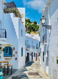 an alley way with tables and chairs on the side, in front of white buildings