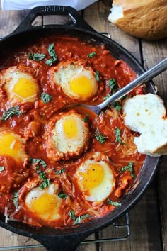 an iron skillet filled with eggs in tomato sauce and parmesan bread on the side