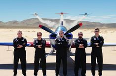 four men standing in front of an airplane with their arms crossed and one man has his mouth open