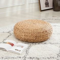 a round wicker ottoman sitting on top of a rug next to an open book