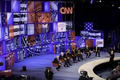 several people sitting on chairs in front of a stage with large television screens behind them