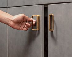 a person's hand is opening the door to a gray cabinet with brass handles