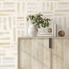 a white vase filled with green plants on top of a wooden dresser next to a wall