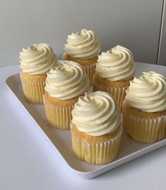 six cupcakes with white frosting on a plate