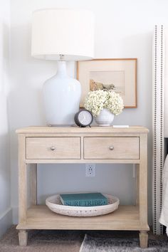 a white vase sitting on top of a wooden table next to a lamp and books