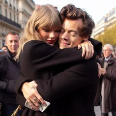 two people hugging each other in front of some people on the street and one person has her arm around the other's shoulder