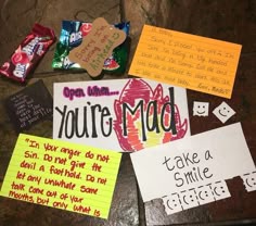 some paper notes are on the table with candy and candies around them that say you're mad, don't give a smile, take a bite