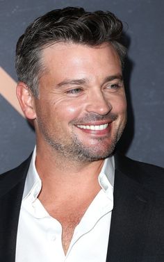 a close up of a person wearing a suit and white shirt smiling at the camera