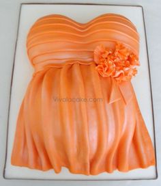 an orange dress cake on a white plate with icing flowers and ribbon around the waist