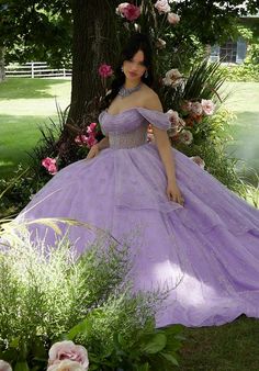 a woman in a purple dress is sitting under a tree with flowers and greenery