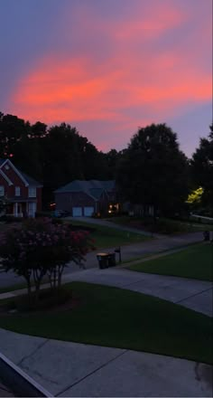 the sky is pink and purple in this neighborhood at dusk, with houses on either side