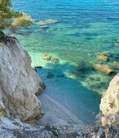 the water is crystal blue and clear at this beach near some rocks with trees on them