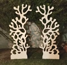 two white sculptures sitting on top of a grass covered field next to a tree and bushes