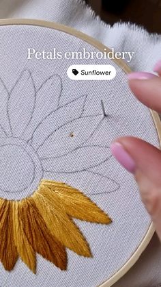 a woman's hand is stitching a flower on a white piece of fabric