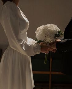 a woman in a white dress holds a bouquet of flowers as a man in a suit stands behind her