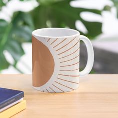 a coffee mug sitting on top of a wooden table next to a book and plant