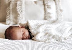 a baby is sleeping under a blanket on a bed with white pillows and blankets around it