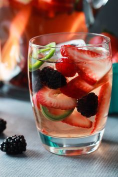 a glass filled with liquid and fruit on top of a table next to berries, cucumber and mint