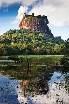 a large rock sitting on top of a lush green hillside next to a body of water