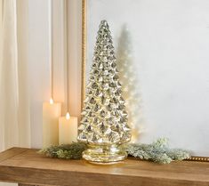 a small christmas tree sitting on top of a wooden table next to a mirror and lit candles