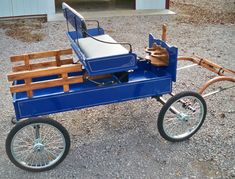 a blue pedal wagon with wooden seats and wheels on gravel area next to garage door