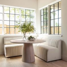 a table with a vase on it in front of two windows and a bench next to it