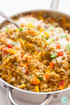 a spoon full of rice and vegetables being lifted from a skillet with a fork