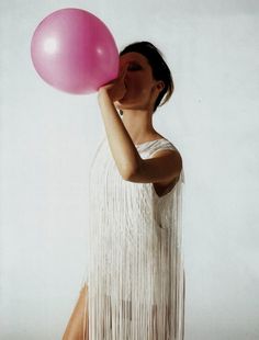 a woman holding a pink balloon in her right hand and wearing a white fringe dress