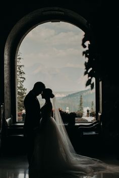 a bride and groom kissing in front of an arched window