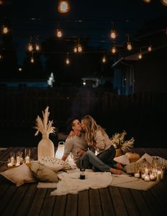 two people sitting on a deck with candles and blankets in front of them, one kissing the other