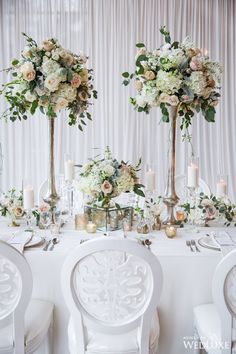 two tall vases filled with flowers sit on top of a table surrounded by white chairs