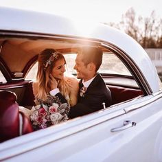 a bride and groom sitting in the back seat of a vintage car looking at each other