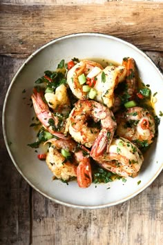 a white bowl filled with cooked shrimp and garnished with herbs on a wooden table