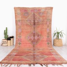 an orange and pink rug with fringes on the floor next to potted plants