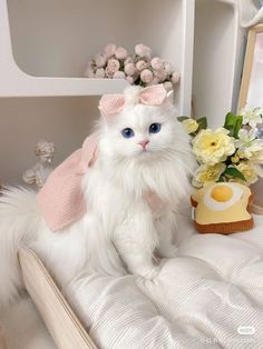 a white cat sitting on top of a bed next to a vase with flowers in it