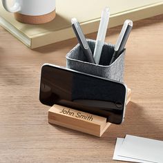 a pen holder with pens and pencils in it on a wooden desk next to a notepad