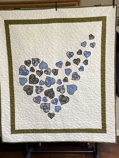 a white quilt with blue and green hearts in the shape of a heart on it