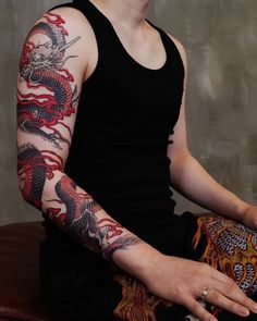 a man with dragon tattoos on his arm sitting down and holding something in his hand