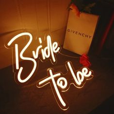 the bride to be neon sign is next to a box with a red rose on it