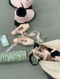 several ballet shoes are laying on the floor next to a cell phone and bag with ribbons