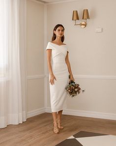 a woman in a white dress standing next to a wall with two lamps on it