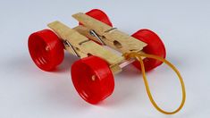 a wooden toy car with red wheels on a white surface, attached to a yellow cord